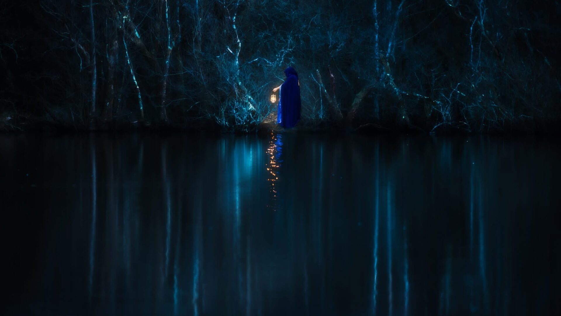 A hooded figure in a blue cloak with a lantern stands on the far side of a lake. The lantern casts light on the water. Trees eerily surround the lake and are reflected in the water.