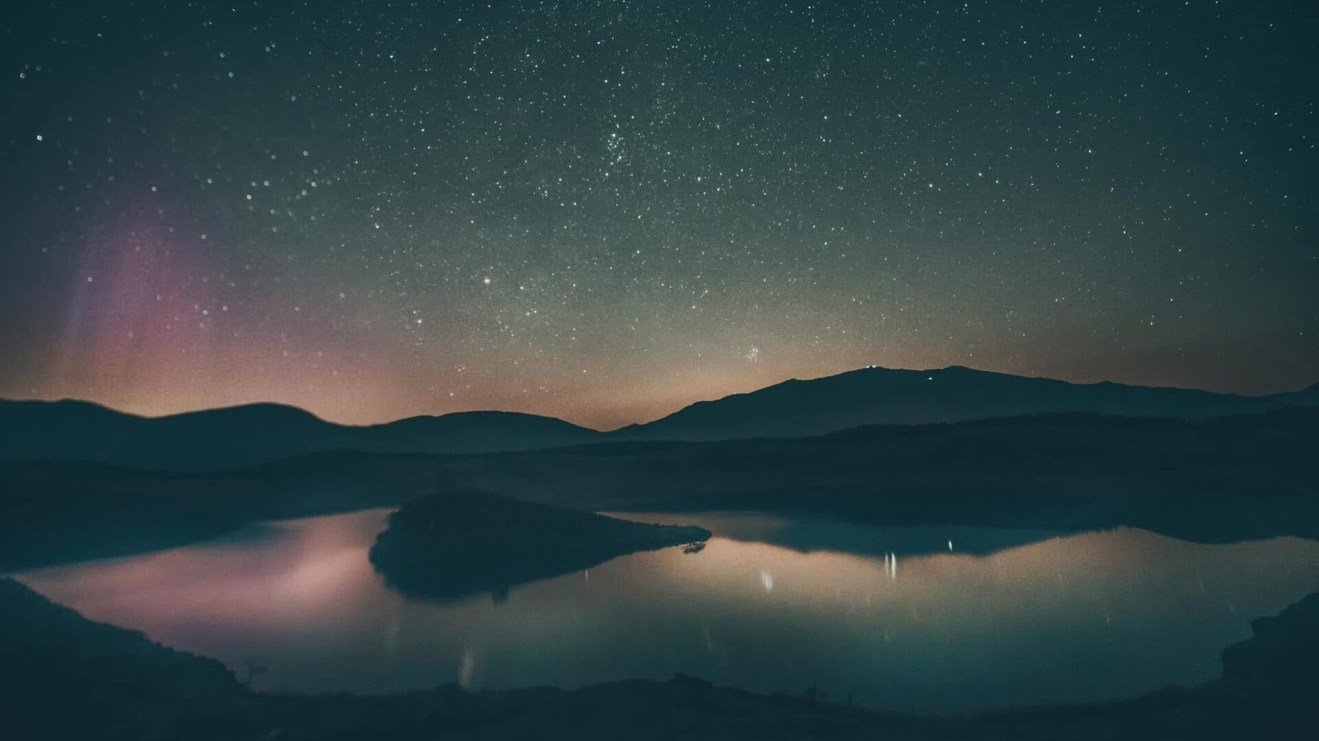 Northern Lights over Llyn y Dywarchen lake in North Wales at night. The stars and aurora are reflected in the water.