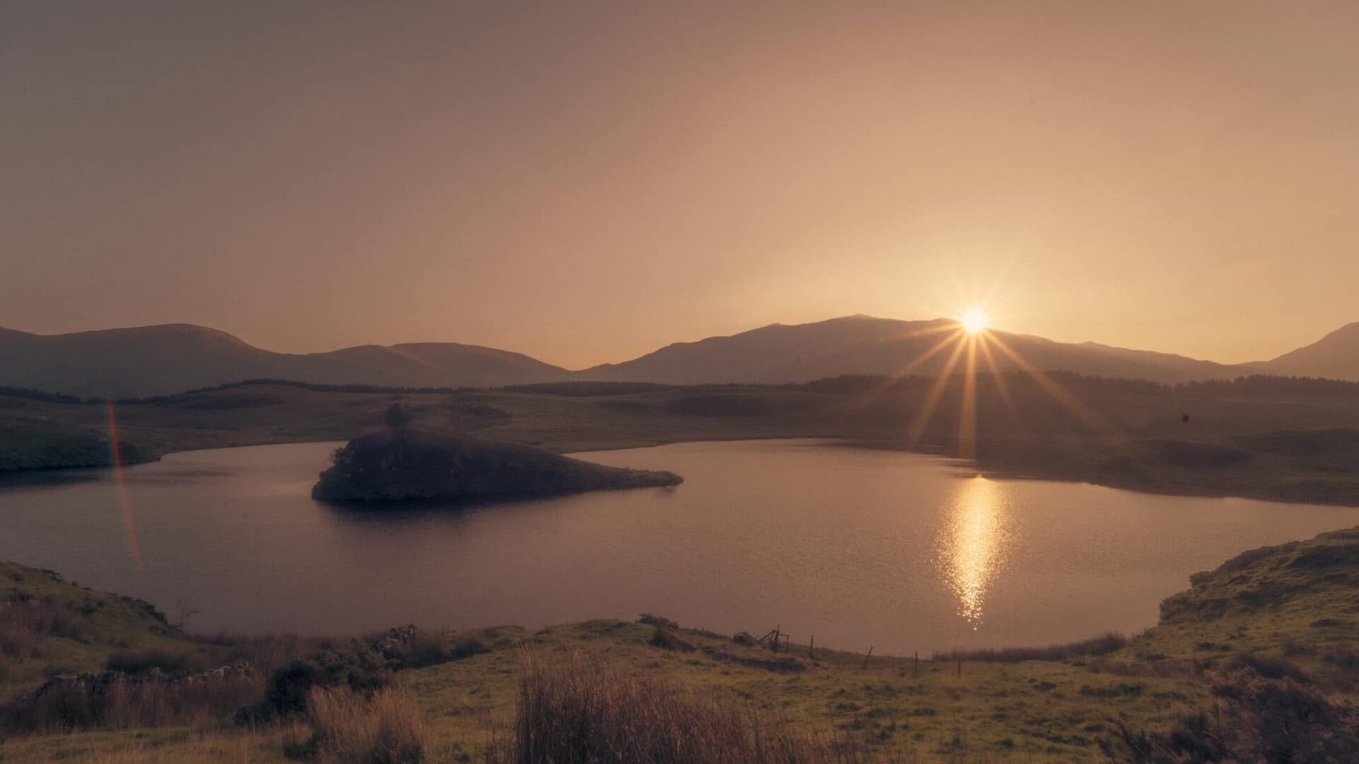 Sunrise at a lake in Wales, Cymru. The sun rays stream from just above the mountain.