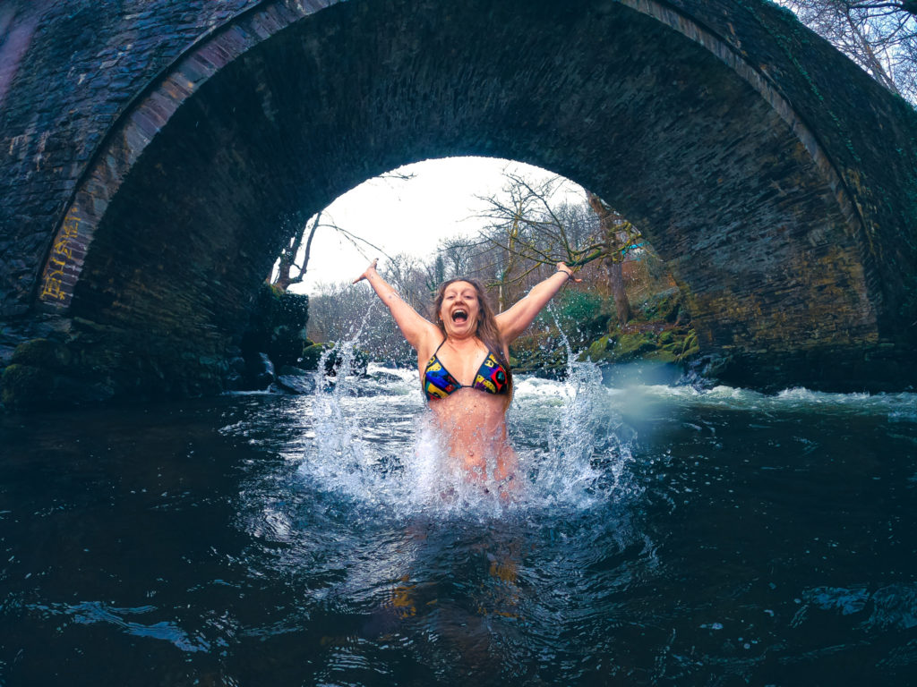 woman in a river jumping in the air with brightly coloured bikini